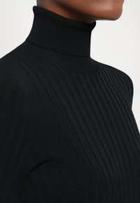 Svart rillede turtleneck genser med en tettsittende design og subtil tekstur, som har vertikale linjer og høy krage.