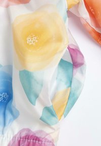 Tissu léger avec un motif floral. Les couleurs incluent le jaune, l'orange, le rose, le bleu et le vert. Présente une texture douce et fluide ainsi qu'un détail élastique.