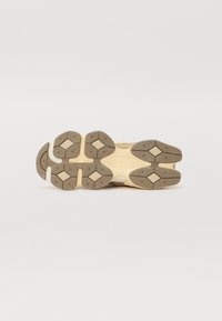 Suola di sneaker con una combinazione di colori beige e marrone chiaro, caratterizzata da una superficie texturizzata, motivi esagonali e una costruzione in gomma resistente.