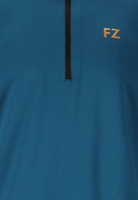 Teepaita, jossa on mustat pystysuorat puolivetoketjut ja kultainen "FZ" -logo vasemmalla rintakehällä.
