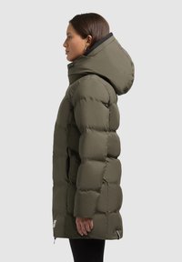 Olivově zelený zateplený kabát s velkou kapucí, který má hladký prošívaný povrch, zapínání na zip a boční rozparky pro snadnější pohyb.