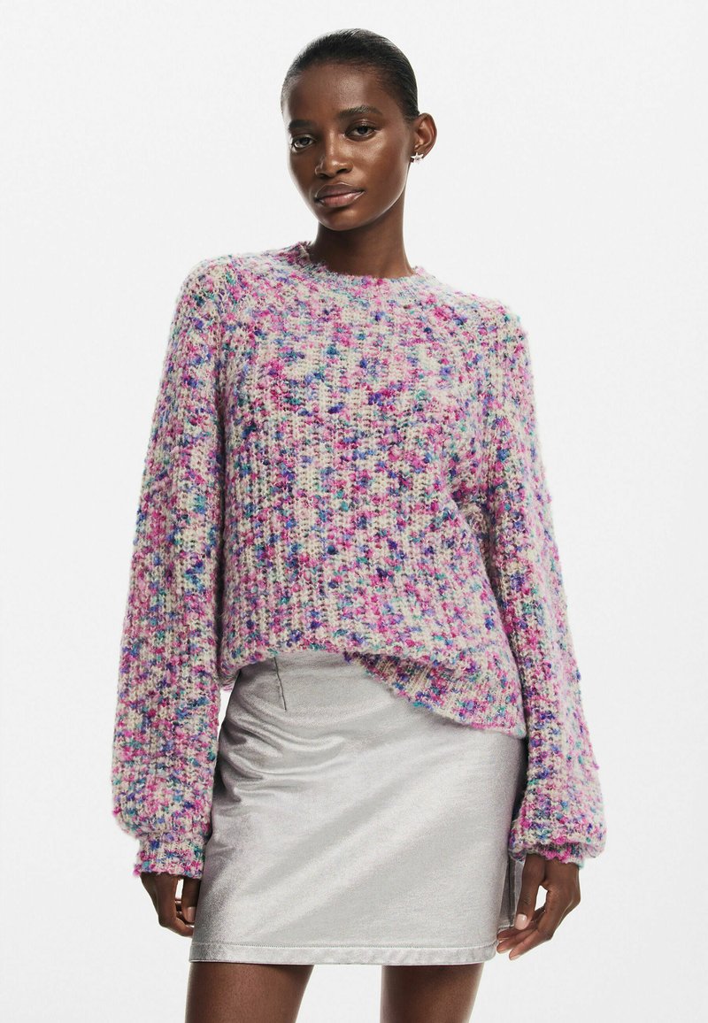 Többszínű, vastag kötésű pulóver rózsaszín, lila és kék árnyalatokban, hosszú ujjakkal és kerek nyakkivágással, ezüst selyem mini szoknyával párosítva.