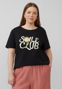 Zwarte t-shirt met een grote crèmekleurige zonafbeelding en de tekst "SOLE CLUB." Het shirt heeft een relaxte pasvorm en een ronde halslijn.