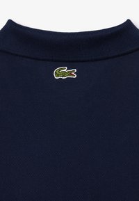 Granatowa koszulka polo z kołnierzykiem z teksturowanej tkaniny, z zielonym haftowanym logo krokodyla na plecach w pobliżu szyi.