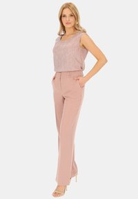 Jasnoróżowy top bez rękawów o delikatnym połysku, zestawiony z beżowymi spodniami o wysokim stanie. Modelka nosi cieliste sandały na obcasie.