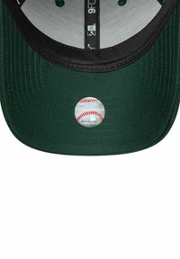 Donkergroene baseballcap met een zwarte klep, voorzien van een metallic logo aan de voorkant. Gelaagd stof met zichtbare stikseldetails.