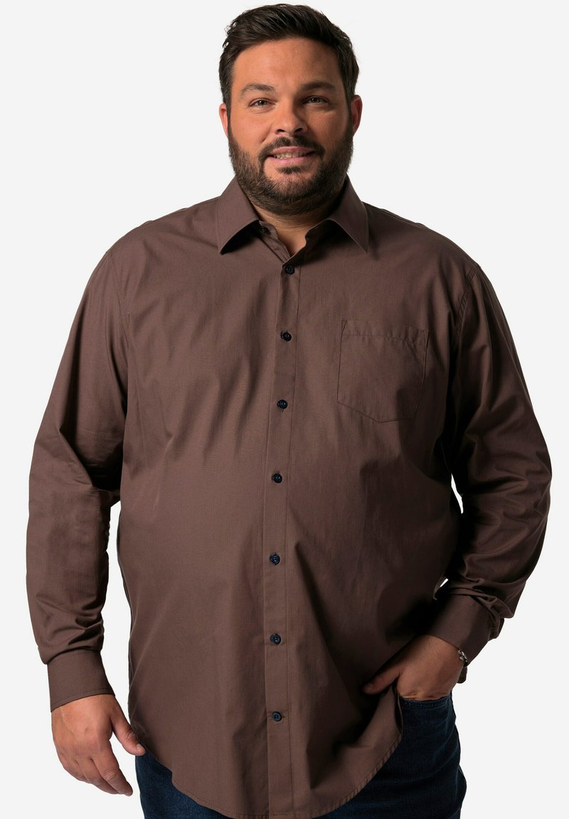Camisa de botones de manga larga marrón con un bolsillo en el pecho, que presenta botones azul oscuro y una textura suave. Combinada con jeans oscuros de mezclilla.