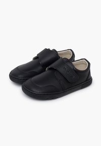 Une paire de chaussures noires pour enfants avec des sangles en velcro et des semelles en caoutchouc texturé, doublure intérieure beige, sur un fond blanc.
