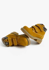 Stivali alla caviglia in suede giallo con due cinturini in Velcro, suola in gomma e accenti grigi nel tallone. Superficie testurizzata e dettagli di cucitura a contrasto.