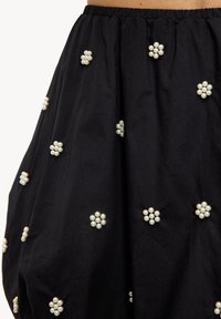 Jupe en tissu noir dotée d'une ceinture élastique froncée et d'un design intégral orné de motifs floraux imitant des perles.
