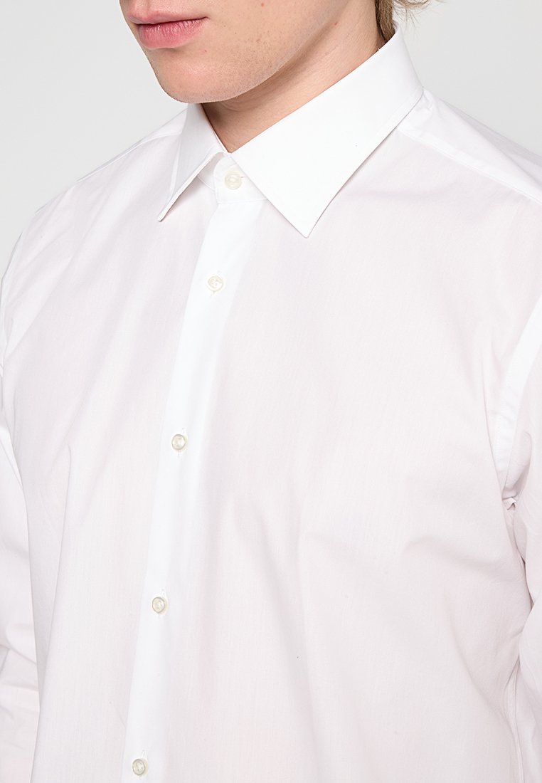 Chemise en coton blanc avec un col classique, un devant boutonné orné de boutons en forme de perles et une texture lisse et légère.