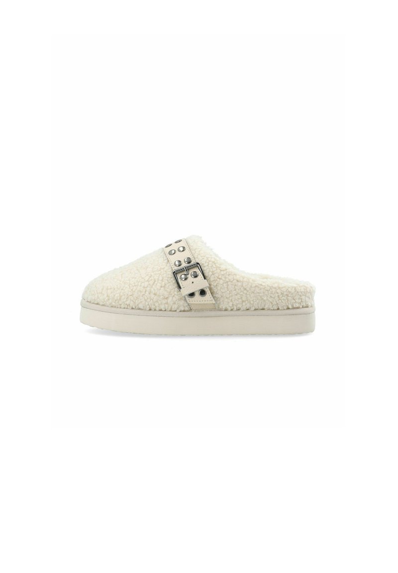 Furry beige slip-on hjemmesko med en tekstureret overdel, der har en rem udsmykket med cirkulære nitter og en flad, lys sål.