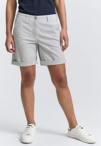 Shorts rayés gris et blanc avec des ourlets roulés, des poches avant et une fermeture à bouton. Assortis avec des baskets blanches sur un fond neutre.
