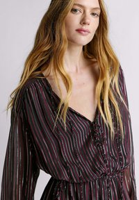 Vestido de manga larga con un escote en V profundo, con rayas verticales multicolores sobre un fondo oscuro y una cintura fruncida con un detalle de lazo.