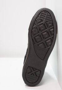 Černá podešev tenisky s geometrickým vzorem, texturovaná guma, kulatý logo a vyvýšené prvky pro lepší přilnavost. Boční profil ukazuje výšku boty.