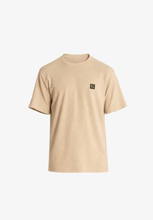 Beige lyhythihainen neulottu T-paita, jossa on pyöreä kaula-aukko ja pieni musta ja kultainen neliönmuotoinen logo vasemmalla rinnassa.