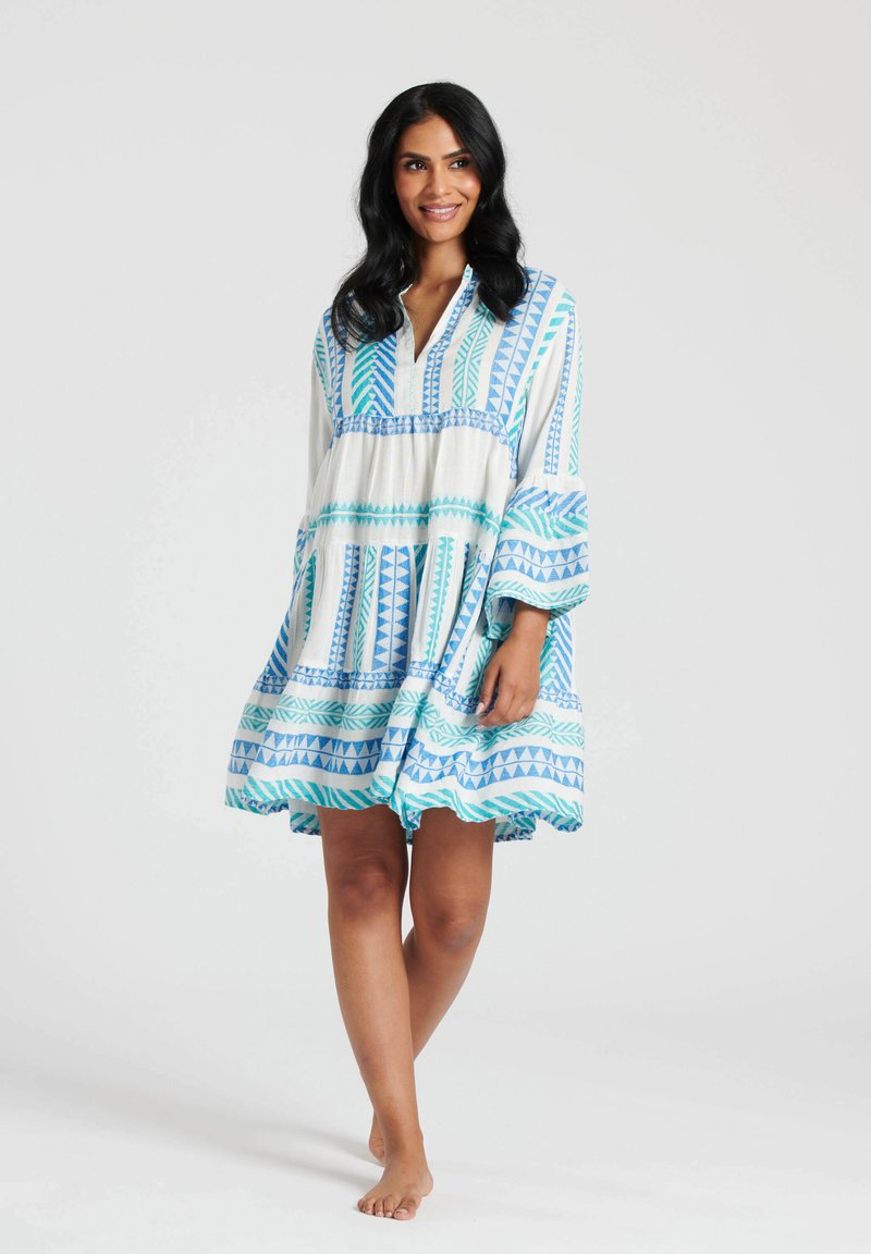 Vestido blanco con patrones geométricos azules, con un corte relajado, mangas largas y escote en V. Tejido ligero y dobladillo en capas.