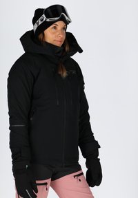 Black insulated ski jacket with a high collar, zippered pockets, and adjustable cuffs, paired with pink ski pants and black gloves.