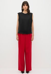 Top nero senza maniche in tessuto morbido abbinato a pantaloni rossi a gamba larga a vita alta. Il modello indossa tacchi neri a punta. Design semplice, senza motivi.