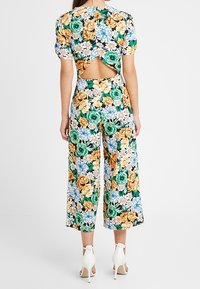 Kwiatowy kombinezon z wielokolorowymi różami i stokrotkami, z otwartym tyłem, krótkimi bufiastymi rękawami i szerokimi nogawkami. Białe szpilki.