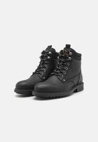 Botas de tobillo de cuero negro con un acabado suave, puntera redondeada, ojales de metal y cordones. Cuenta con un collar acolchado y una suela de goma duradera.