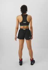 Crna sportska majica s racerback dizajnom, s neon zelenim detaljem. Uparena s crnimSHORTS i tamnoplave obuće s crvenim akcentima.