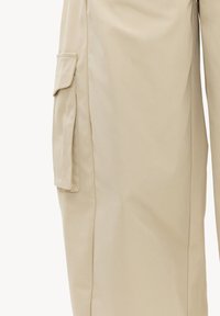 Pantalon cargo beige avec une poche latérale munie d'un rabat et d'un détail zippé sur la jambe gauche.