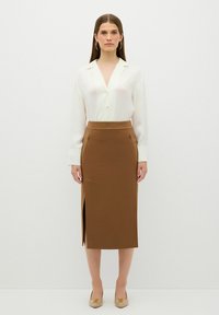 Witte sheer blouse met een kraag, gecombineerd met een bruine, aansluitende midi-rok met een zijsplit en twee zakken aan de voorkant.