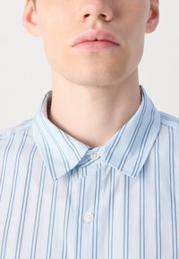 Cămașă cu guler de culoare albastru deschis, decorată cu dungi verticale de un albastru mai închis, cu un guler cu nasturi și un material ușor texturat.