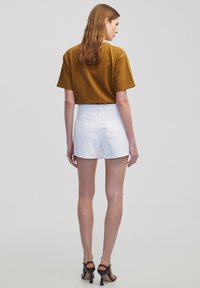 Brune korte mouwen top gecombineerd met witte denim shorts. De shorts hebben achterzakken en een gladde textuur, aangevuld met zwarte haksandalen.