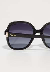 Polaroid black oversized sunglasses with gradient purple lenses. Wide rectangular frames feature metallic accents and bold hinge detailing.