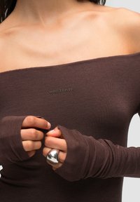 Top marrone off-the-shoulder realizzato in tessuto a coste, con maniche lunghe dotate di aperture per il pollice e un piccolo logo ricamato sul petto.