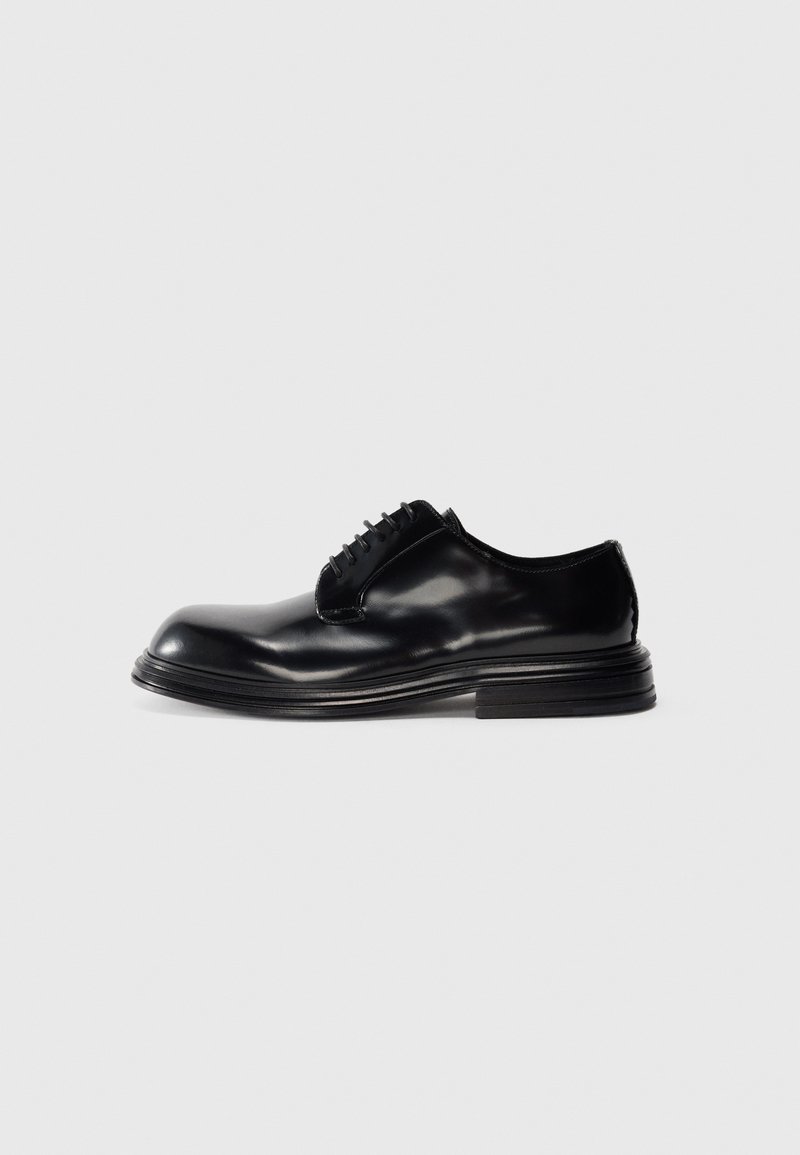 Zapatos de vestir de cuero negro con punta redonda, acabado liso, diseño de cordones y tacón apilado. Estilo minimalista sin logotipos visibles.