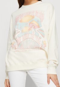 Svetle béžová mikina s grafickým návrhem barevných hub a textem, s pružnými manžetami a lemem pro pohodlný střih.