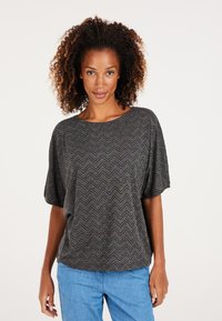 Grå top med et fiskebensmønster, korte brede ærmer og rund halsudskæring, lavet af et tekstureret stof. Sammen med lyseblå bukser.