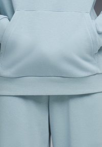 Világoskék pulóverkapucnis felső és hozzá illő nadrág puha anyagból, elöl zsebbel, bordázott passzékkal az ujjánál és a szegélyénél. Simulékony textúra és egyszerű dizájn.