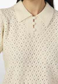 Maglione lavorato a maglia color crema con un motivo a diamante, con colletto e tre bottoni testurizzati sul davanti.
