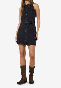 Černé džínové šaty bez rukávů s knoflíkovou přední částí, se staženým pasem a kapsami. Má rovný střih a měkkou texturu. Hnědé kozačky do kolen.