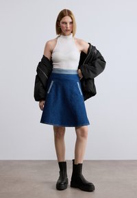 Φούστα σε σχήμα Α από τζιν, σκούρο μπλε, με γαλάζια μέση και δύο τσέπες ως διακοσμητικά στοιχεία. Συνδυάζεται με λευκό ριμπ μπλουζάκι και μαύρο μπουφάν bomber.