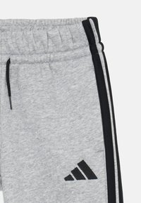 Gray sweatpants with a drawstring waist, black side stripes, a textured fabric, and a black logo near the hem.