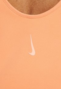 Top atlético color durazno con escote en forma de u y tela suave. Presenta un pequeño logo blanco de Nike en el pecho.
