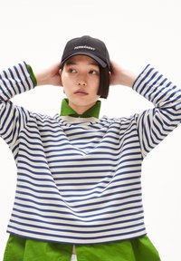 Top in cotone a righe con strisce orizzontali blu e bianche, con colletto verde e vestibilità rilassata. Cappellino nero con la scritta "PERMANENT".
