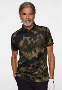 Kortärmad polo i mörkgrön och svart med camouflage-mönster. Har en klassisk krage och knappslå. Mjukt tyg.