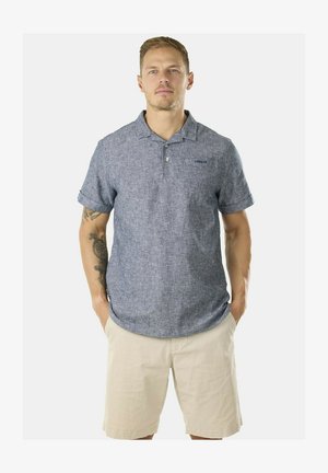 Polo shirt a maniche corte in tessuto blu texturizzato; presenta un colletto, una tasca sul davanti e maniche arrotolate, abbinato a pantaloni corti beige chiaro.