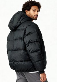 Veste matelassée noire avec capuche, dotée d'un design matelassé, de poignets élastiques et d'un ourlet à cordon de serrage pour une meilleure chaleur et un meilleur ajustement.