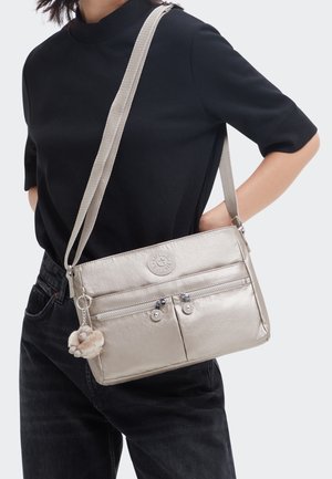 Sac à bandoulière en métal argenté avec deux poches zippées, détail de logo et un charme en peluche. Dispose d'une bandoulière durable et d'une texture lisse et soyeuse.