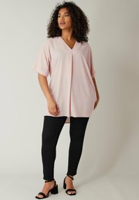 Jasnoróżowa bluzka w serek z krótkimi rękawami, luźny krój i detale w formie fałd, zestawiona z czarnymi wąskimi dżinsami i czarnymi sandałkami na obcasie.