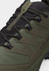 Nahaufnahme eines olivgrünen und schwarzen Wanderschuhs mit verstärkter Schnürung und strukturiertem Mesh-Obermaterial, mit "La Sportiva"-Markenaufdruck.