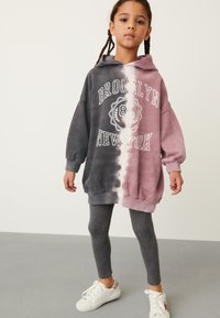 Bluza z kapturem z gradientem kolorów od czarnego do różowego, z napisem "BROOKLYN". Połączona z szarymi legginsami i białymi trampkami.