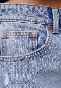 Ljusblå denimjeans har kontrasterande sömmar, en liten bakficka, slitna detaljer och en hög midje-design.